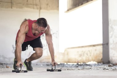 Kaslı, atletik, terk edilmiş bir binada şınav çeken genç bir adam.