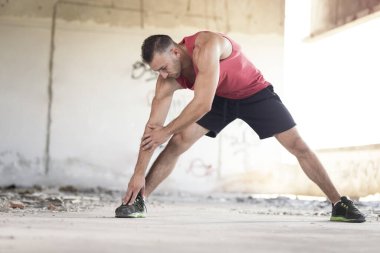 Kaslı, atletik yapılı, spor yapmadan önce harabe bir binada uzanan genç bir adam.