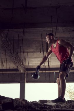 Genç, kaslı, atletik yapılı bir adamın, terkedilmiş bir binada ağırlık kaldırışının yan görüntüsü.