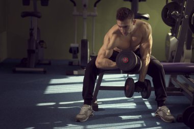 Bir spor salonunda egzersiz, bir halter makine üzerinde oturan ve iki halter kaldırma sporcu genç kas inşa