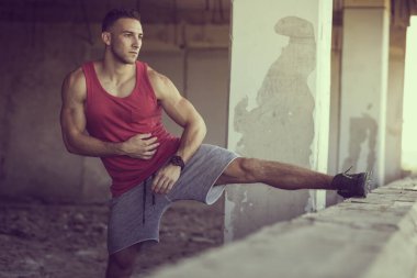 Kaslı, atletik yapılı, spor yapmadan önce harabe bir binada uzanan genç bir adam.