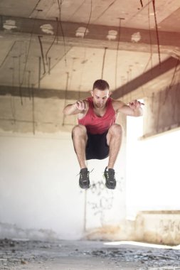 Genç, atletik, kaslı bir adam terk edilmiş bir buinlding 'de sıkı bir çalışmanın parçası olarak atlıyor.