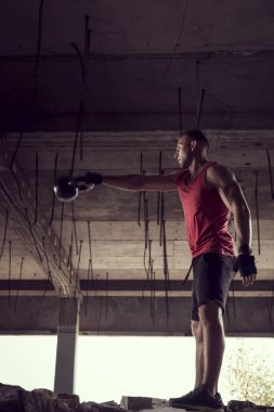 Terk edilmiş bir binada ağırlık kaldıran genç, kaslı bir sporcunun yan görünüşü.
