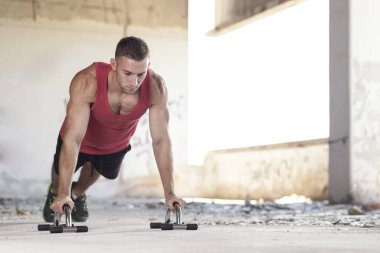 Kaslı, atletik, terk edilmiş bir binada şınav çeken genç bir adam.