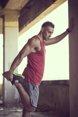 Kaslı, atletik yapılı, spor yapmadan önce harabe bir binada uzanan genç bir adam.