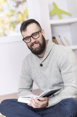 Adam yerde oturuyor, kitap okuyor ve evde dinleniyor.