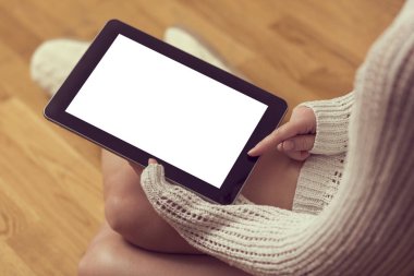 Ahşap zeminde oturan, süveter ve çizme giyen ve tablet bilgisayar kullanan güzel bir kadının ayrıntıları. İşaret parmağına odaklan.