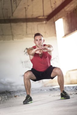 Kaslı, atletik yapılı, spor yapmadan önce harabe bir binada uzanan genç bir adam.