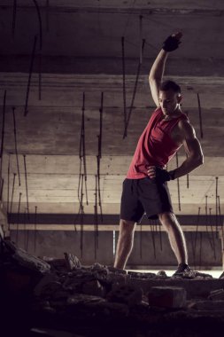 Kaslı, atletik yapılı, spor yapmadan önce harabe bir binada uzanan genç bir adam.