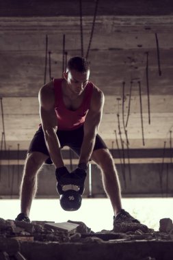 Genç, kaslı bir sporcunun, terkedilmiş bir binada ağırlık kaldırışının ön görüntüsü.