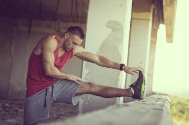 Kaslı, atletik yapılı, spor yapmadan önce harabe bir binada uzanan genç bir adam.