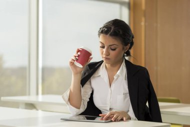 Genç bir iş kadını ofisinde oturmuş, kahve içiyor ve yeni bir proje planlıyor.