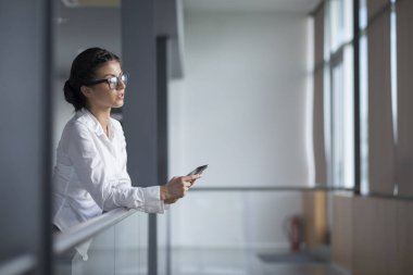 Güçlü, kendinden emin, iş kadını elinde tablet bilgisayarla bir ofis binasında duruyor.