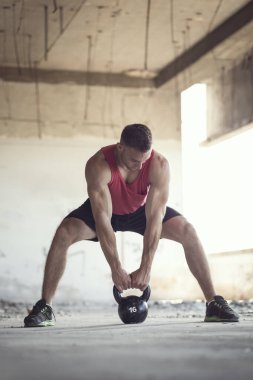 Terk edilmiş bir binada spor yapan bir sporcu, ağırlık kaldırıyor.