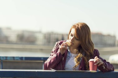 Genç, güzel bir esmer, merdivenlerde duruyor, kahve içiyor, kurabiye yiyor, tablet bilgisayarda internette sörf yapıyor ve güneşli bir günün tadını çıkarıyor.