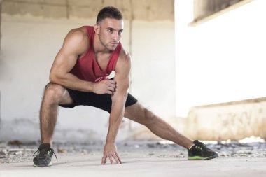 Terk edilmiş bir harabe binada spor eğitiminden önce kaslı sporcu esniyor.