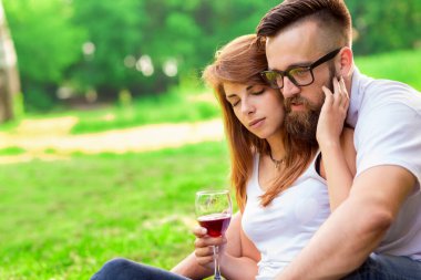 Birbirine aşık çiftler parkta bir piknik battaniyesinde oturmuş ellerinde şarap kadehleri, sarılıyorlar ve birlikte vakit geçiriyorlar.