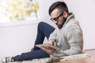 Yerde yatan bir adam, elinde bir tablet bilgisayarla e-kitap okuyor.