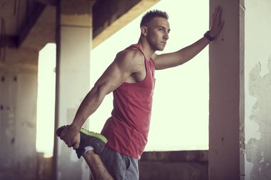 Kaslı, atletik yapılı, spor yapmadan önce harabe bir binada uzanan genç bir adam.