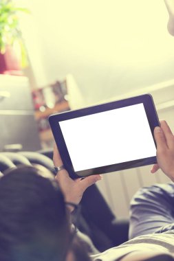 Oturma odasındaki kanepede uzanmış, tablet bilgisayarda internette sörf yapan bir erkek model.