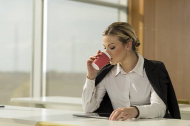 Masada oturan bir kadın bir fincan kahve içiyor.