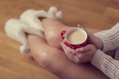 Ellerinde kahve, beyaz bir süveter ve çizme giyen ve boş zamanların tadını çıkaran bir kadının ellerini kapat.