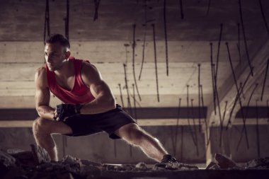 Kaslı, atletik yapılı, spor yapmadan önce harabe bir binada uzanan genç bir adam.