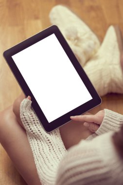 Ahşap zeminde oturan, süveter ve çizme giyen ve tablet bilgisayar kullanan güzel bir kadının ayrıntıları.