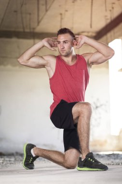 Kaslı, atletik yapılı, spor yapmadan önce harabe bir binada uzanan genç bir adam.