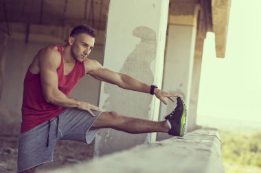 Kaslı, atletik yapılı, spor yapmadan önce harabe bir binada uzanan genç bir adam.