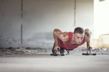 Kaslı, atletik, terk edilmiş bir binada şınav çeken genç bir adam.