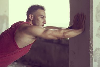 Kaslı, atletik yapılı, spor yapmadan önce harabe bir binada uzanan genç bir adam.