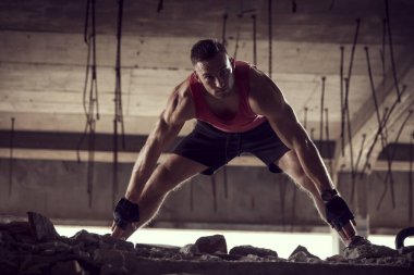 Kaslı, atletik yapılı, spor yapmadan önce harabe bir binada uzanan genç bir adam.