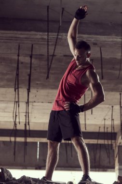 Kaslı, atletik yapılı, spor yapmadan önce harabe bir binada uzanan genç bir adam.