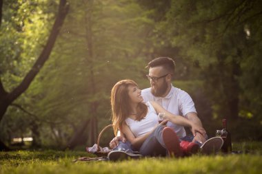 Çift üzerinde bir park piknik battaniyeye oturmuş, Birbirinizle konuşmak, şarap içme ve doğa güzel, huzurlu bir günde zevk aşık