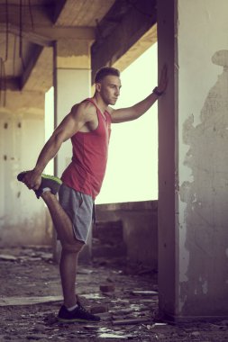 Kaslı, atletik yapılı, spor yapmadan önce harabe bir binada uzanan genç bir adam.