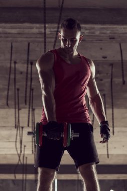 Genç kaslı sporcu, dambılla çalışıyor, terkedilmiş bir binada ağırlık kaldırıyor.