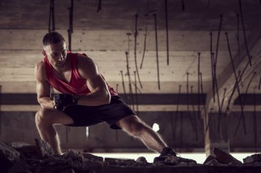 Kaslı, atletik yapılı, spor yapmadan önce harabe bir binada uzanan genç bir adam.