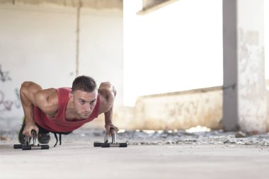 Kaslı, atletik, terk edilmiş bir binada şınav çeken genç bir adam.