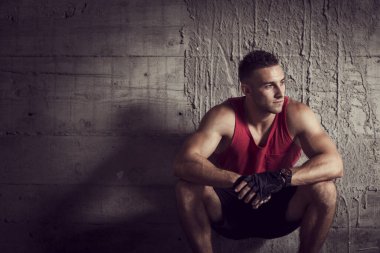 Genç kaslı sporcu, terk edilmiş bir binanın beton duvarının yanında çömelmiş, sıkı çalışmaya ara veriyor.