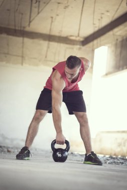 Genç, kaslı bir sporcunun, terkedilmiş bir binada ağırlık kaldırışının ön görüntüsü.
