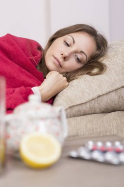 Yatağında battaniyeyle yatan hasta kadın yüksek ateş ve grip. İlaçlar, çaydanlık ve limon masada.