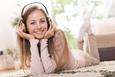 Güzel esmer kız dairesinin zemininde uzanıyor, müzik dinliyor ve boş zamanlarının tadını çıkarıyor.