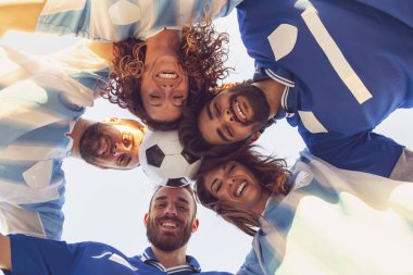 Bir grup futbol fanatiğinin dar açılı görüntüsü, çember şeklinde toplanmış ve kafalarıyla bir top tutuyorlar.