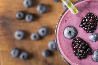 Kırsal bir masaya yerleştirilmiş bir bardaktaki yabanmersinli smoothie 'nin üst görüntüsü.