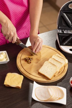 Kadın ellerinin kesme tahtasındaki sandviçler için zeytin keserken yüksek açılı görüntüsü kahvaltıda sandviç makinesinde sıcak sandviç yapan kadın. Ucuna odaklan, bıçağa odaklan.