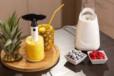 Ananas kesiciyle soyulmuş bir ananasın yüksek açılı görüntüsü mutfak tezgahında Bledner 'ın yanında. Yabanmersinine ve ananasa odaklan.