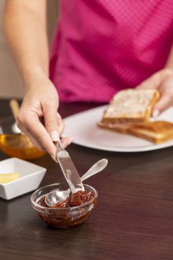 Kadın eli, mutfak bıçağıyla reçel alıp kahvaltıda reçelli ve tereyağlı sandviç yapıyor. Bıçağın ucuna odaklan.
