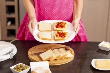 Sandviç makinesinde ısıtılmaya hazır sandviçleri olan bir kadın kahvaltı için sıcak sandviç hazırlıyor.