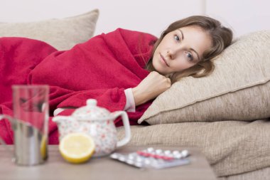 Yatağında battaniyeyle yatan hasta kadın yüksek ateş ve grip. İlaçlar, çaydanlık ve limon masada.